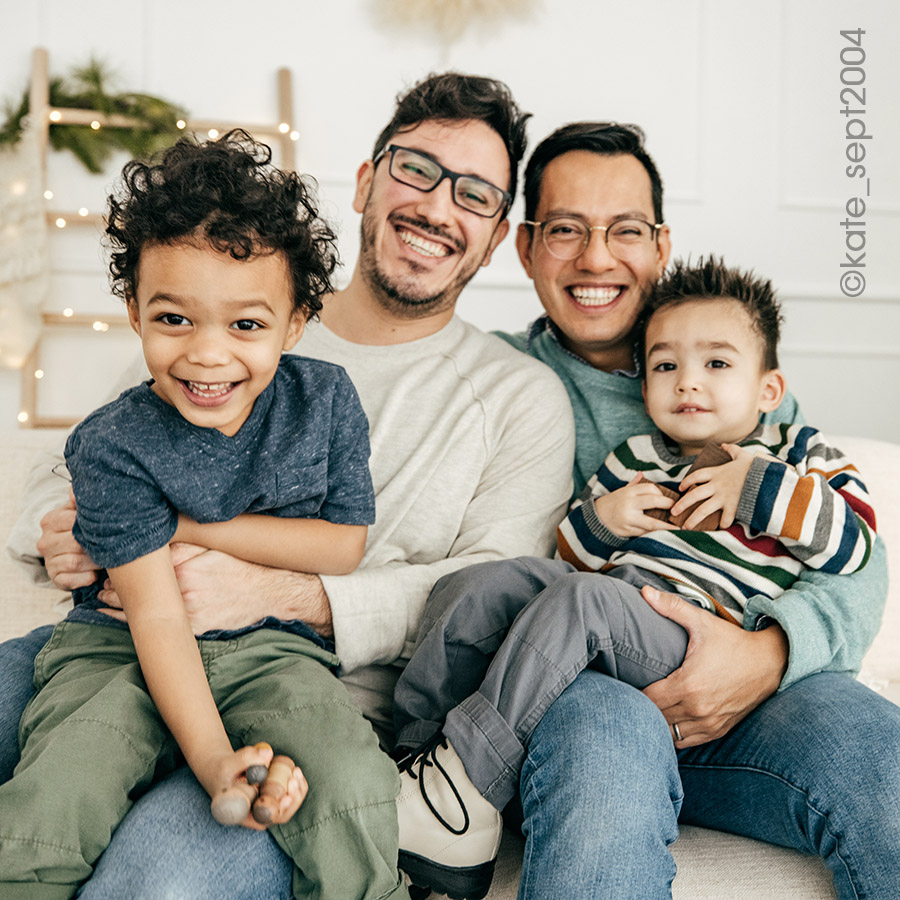 two adult males posing on a sofa with their two sons