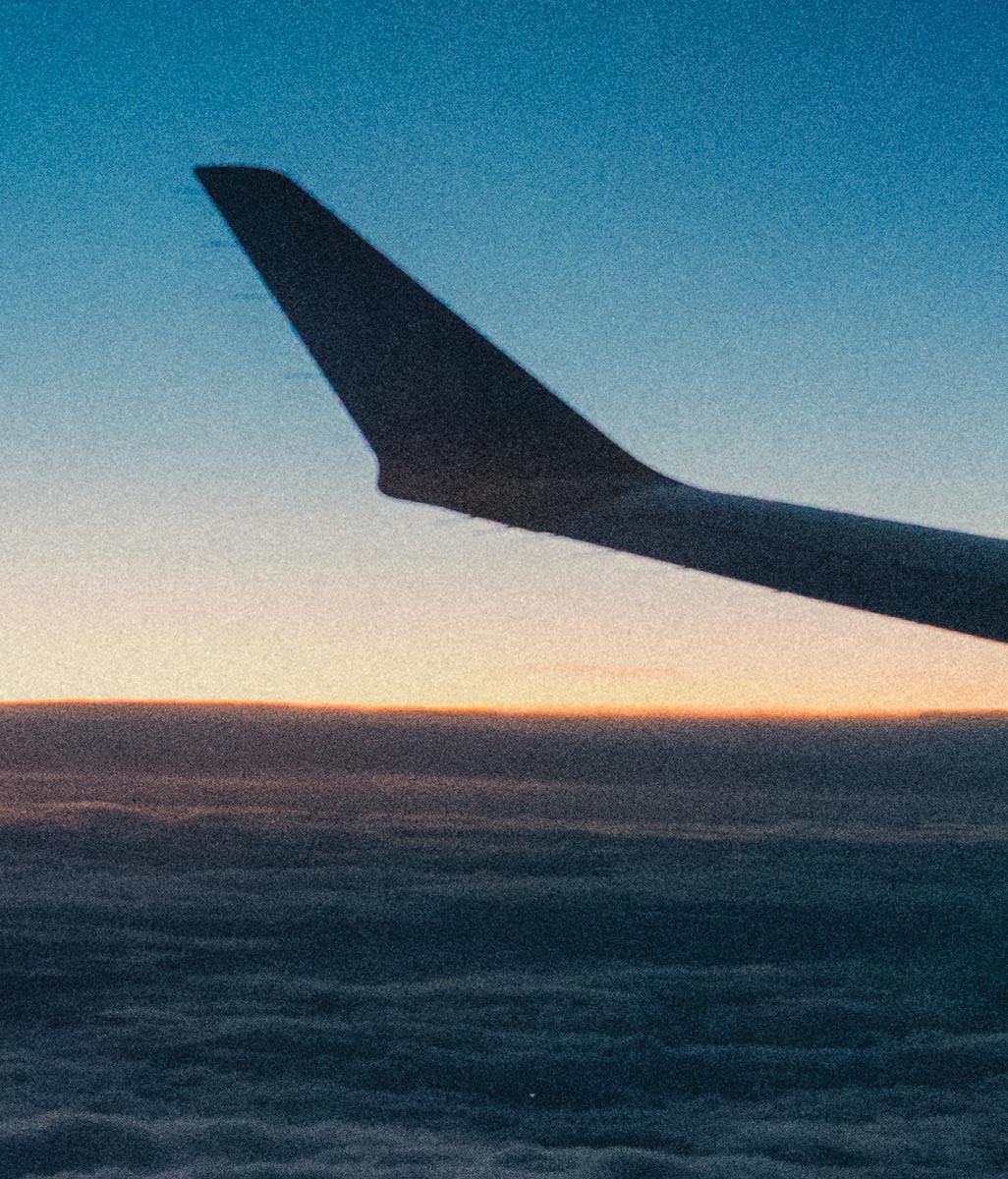 port wing of an airplane as seen from a window seat with sunrise on the horizon
