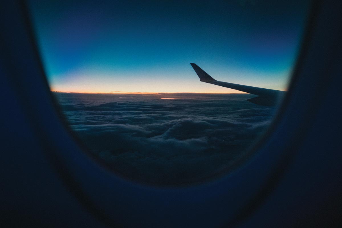 port wing of an airplane as seen from a window seat looking onto a sunrise
