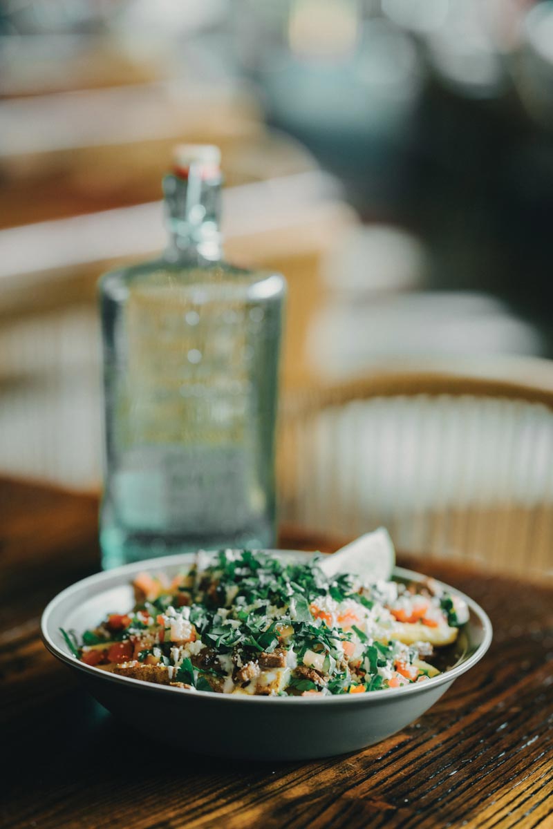 a healthy looking bowl of vegetables over potatoes along with a glass bottle of water on a wooden table