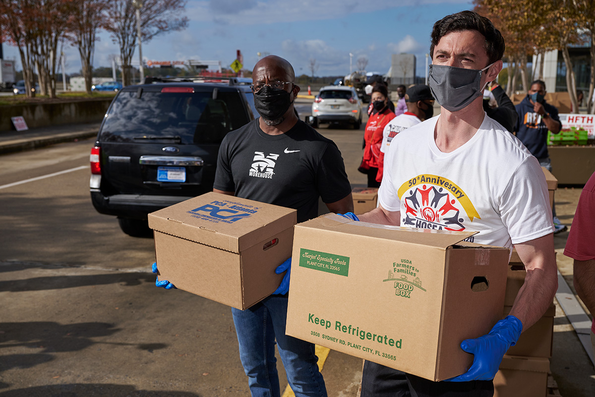 Then-senate candidates Rev. Raphael Warnock and Jon Ossoff hold boxes of food to give away at the 2020 Hosea Feed the Hungry and Homeless 50th Anniversary event Nov. 26, 2020.