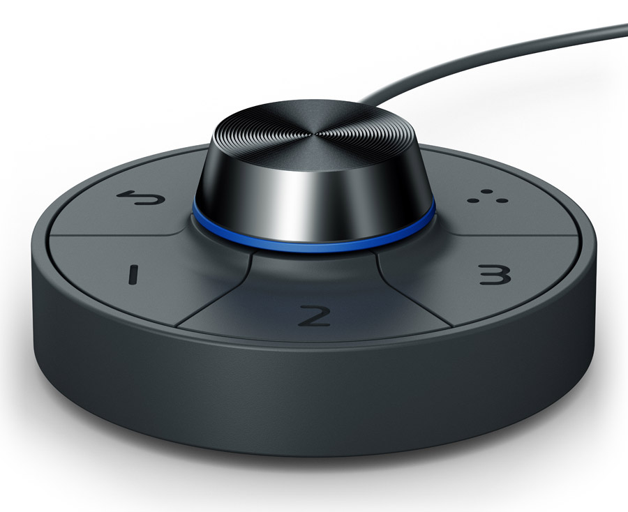 A BenQ Hotkey Puck G2 monitor controller, which is black and shaped similarly to a hockey puck with a central dial and buttons around the perimeter