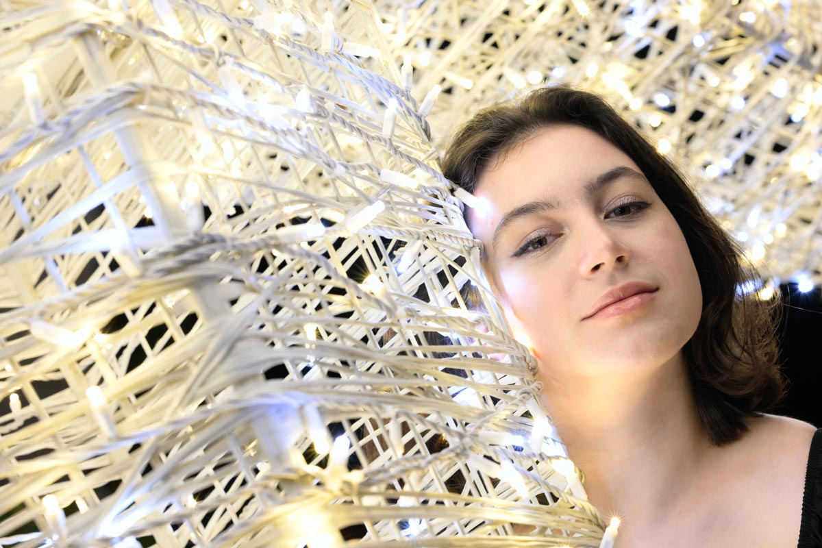 Young woman with dark hair, head and shoulders portrait, posing next to decorative string lights