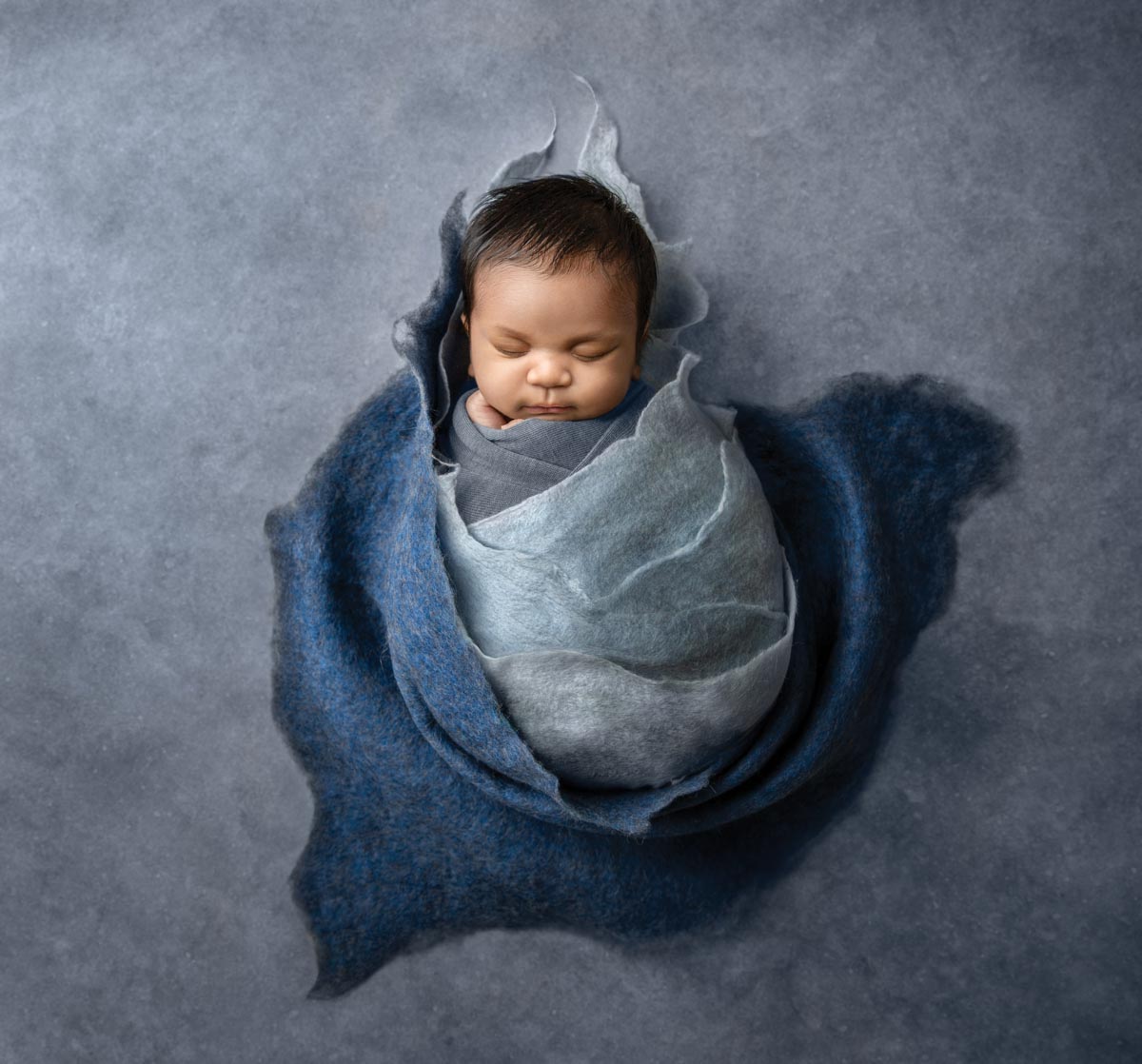 newborn baby wrapped in light blue and navy blue felt fabric