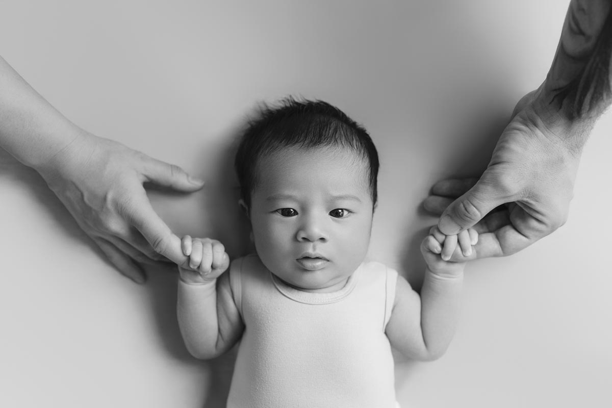 black-and-white photo of a newborn holding parents' hands