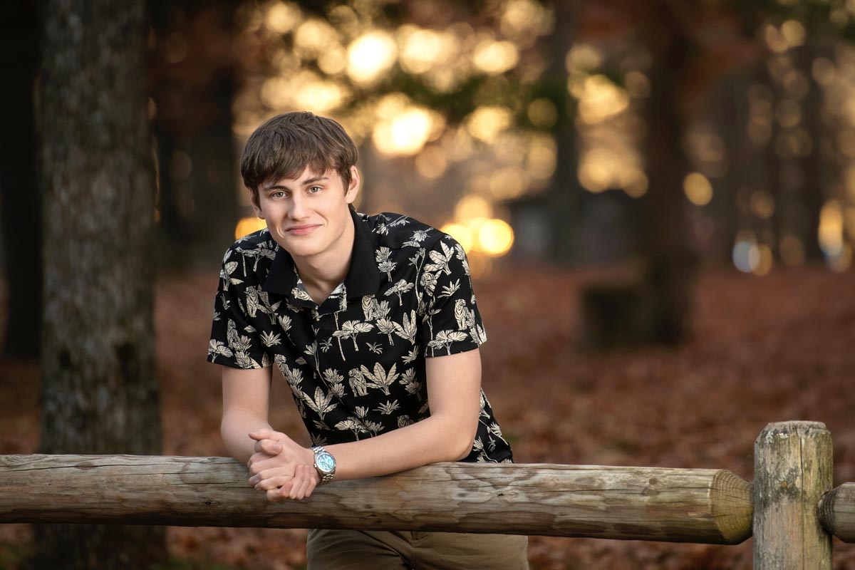high school senior portrait by Kristina Carlson of a boy with his arms propped on a fence
