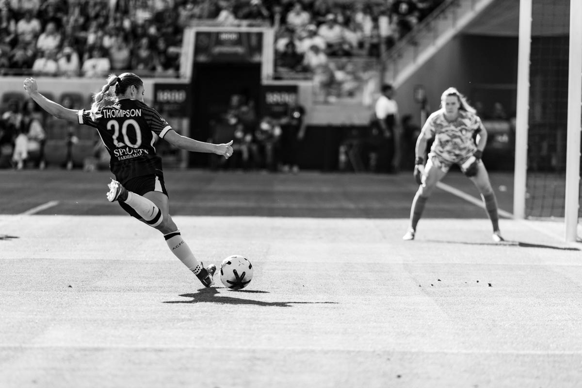 Angel City FC player taking a shot on goal with goalie crouching and facing her in the background