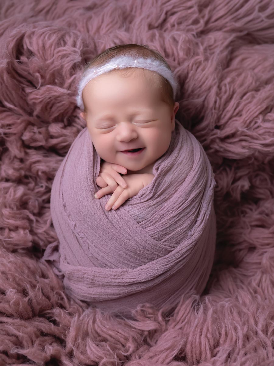 portrait of a smiling newborn swaddled in mauve