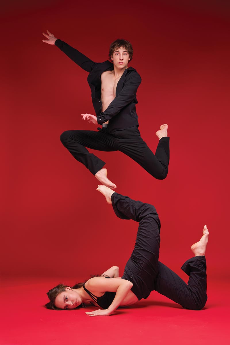two dancers, one leaping in the air and the other on the floor, with their feet touching