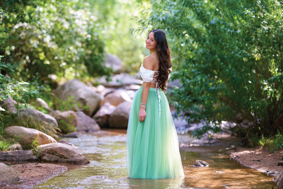 senior portrait of a girl in a long teal skirt standing in a stream
