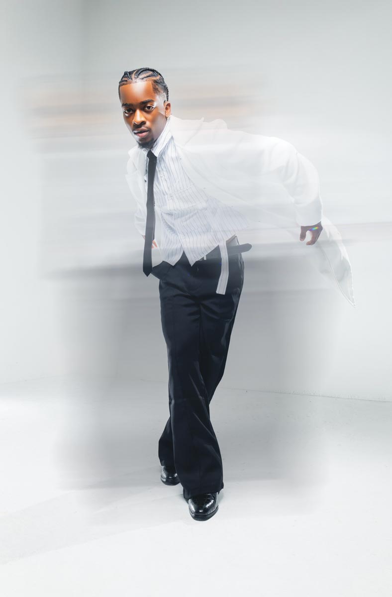 blurred movement of a male subject wearing a white and black striped button down shirt, a black tie, a white jacket, and black slacks on a white background