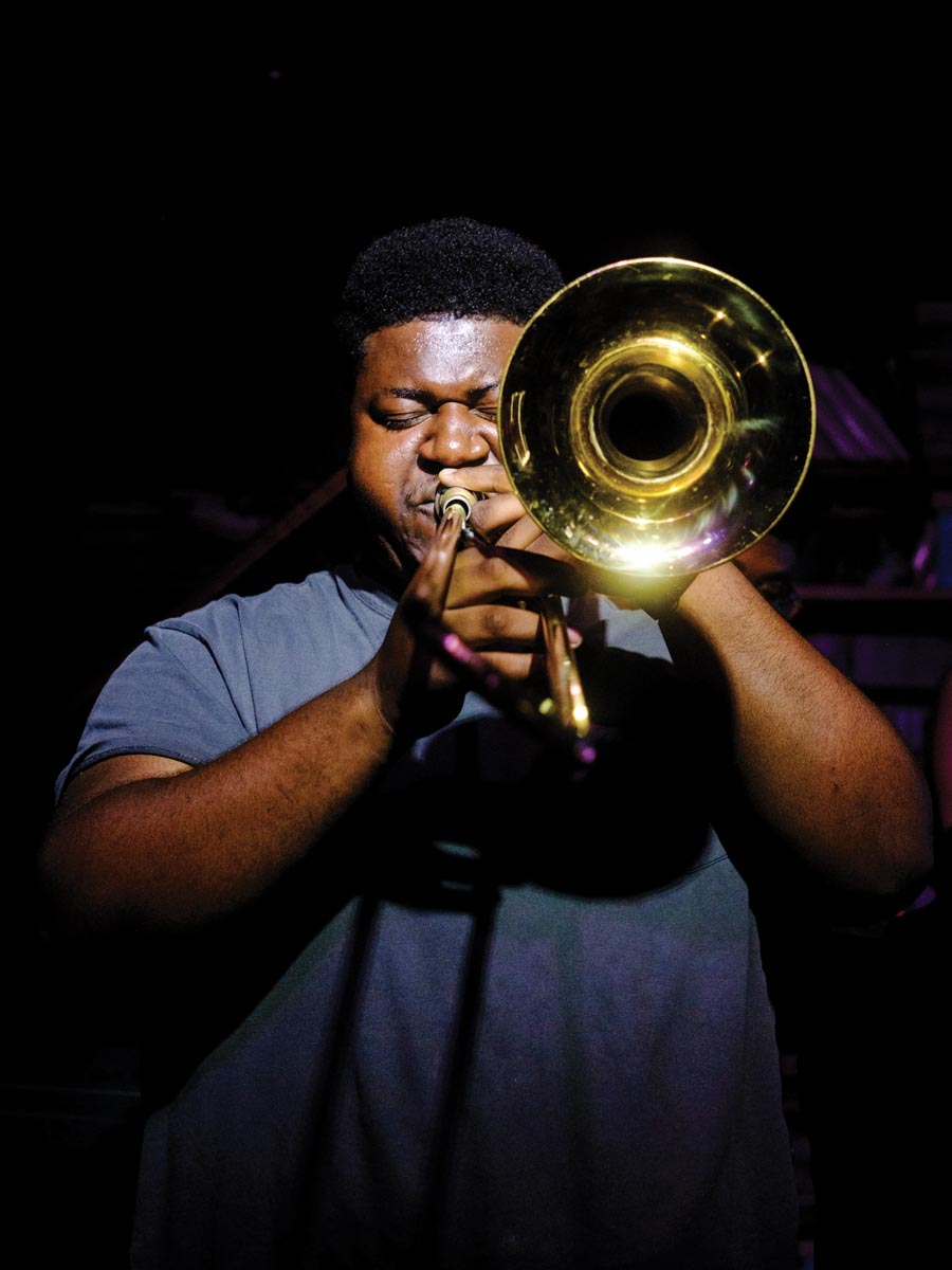 man playing horned instrument on a black background with eyes closed