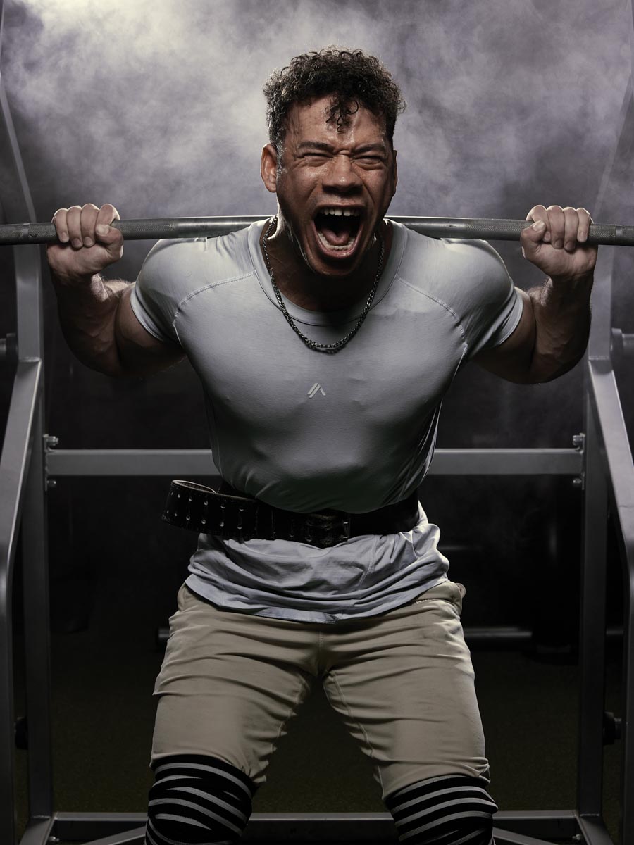 man screaming while lifting a barbell, with smoke in the background