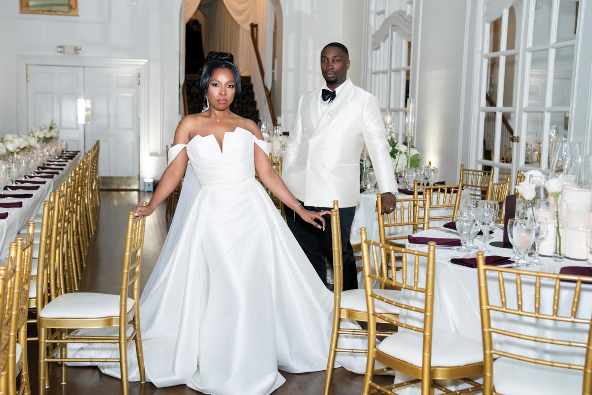 bride and groom in ballroom with gold chairs and white tablecloths