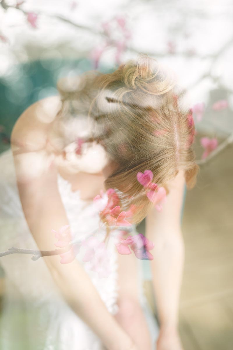 girl wearing white dress bending over with pink flowers in foreground