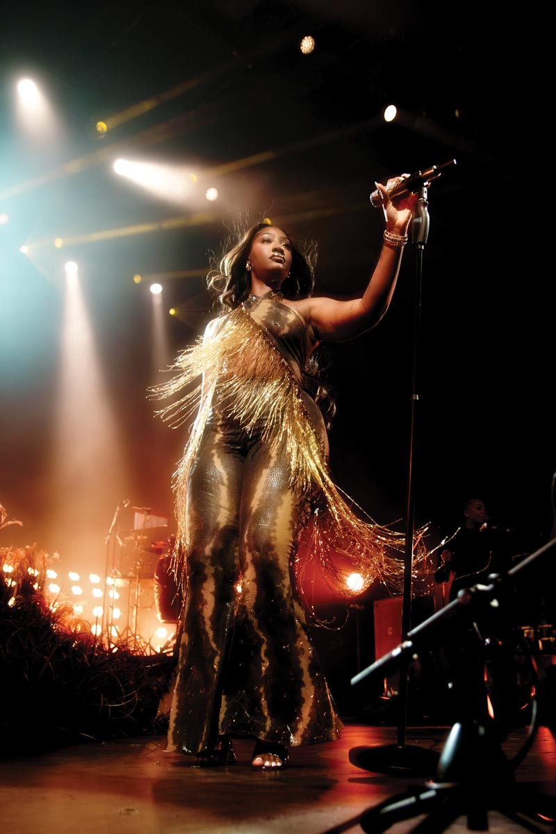 a female singer on a stage at the microphone wearing a gold outfit