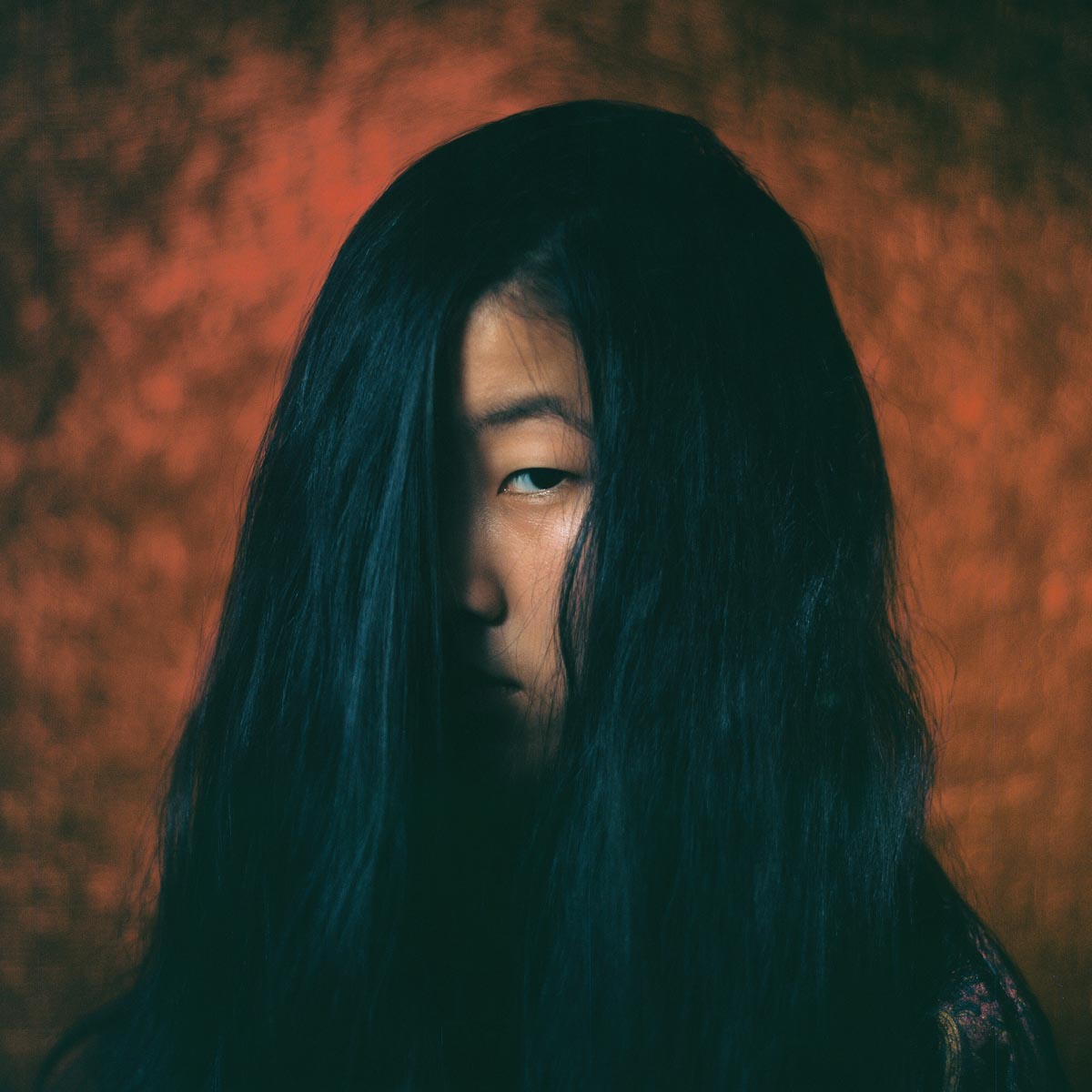a young person with long black hair covering most of their face except one eye and cheek
