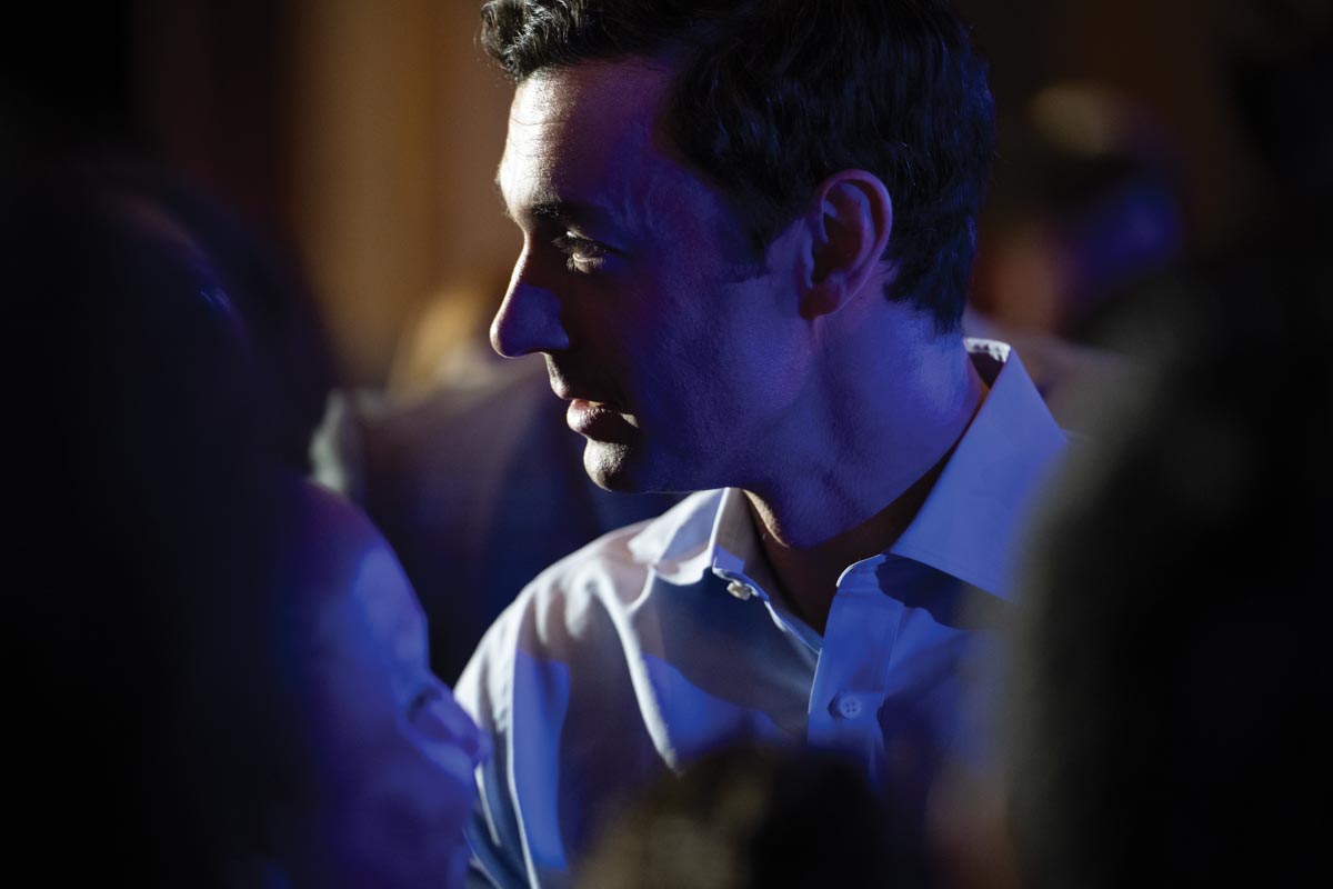 U.S. Senator Jon Ossoff (D-GA) in profile in a dimly lit room with brighter light on the far side of his face, and a blue light on the near side of his face. He is wearing a white button-down shirt.