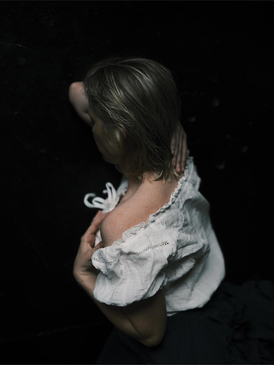 an overhead shot of a woman in a white off-the-shoulder top on a black background