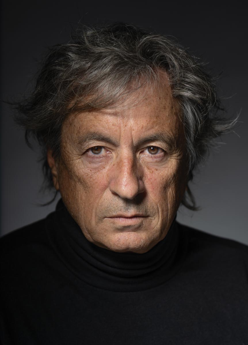 Portrait of a mature man wearing a black turtleneck against a gray backdrop
