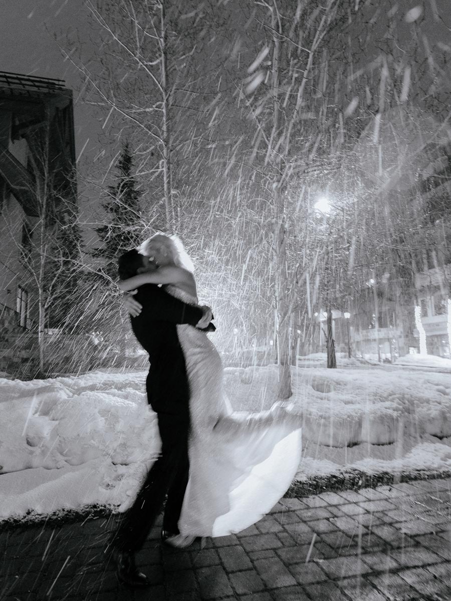 black and white photo of groom holding up bride as the snow falls