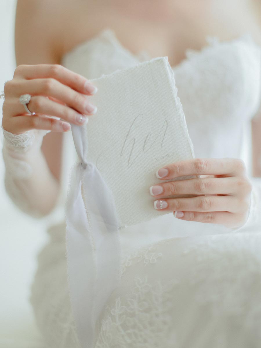 closeup of bride's hands holding wedding invitation while wearing wedding dress