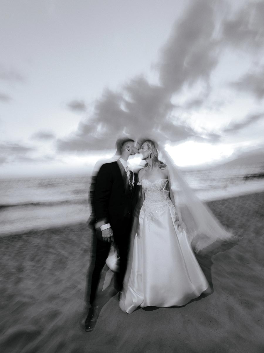 blurry black-and-white photo of bride and groom on the beach in front of the ocean