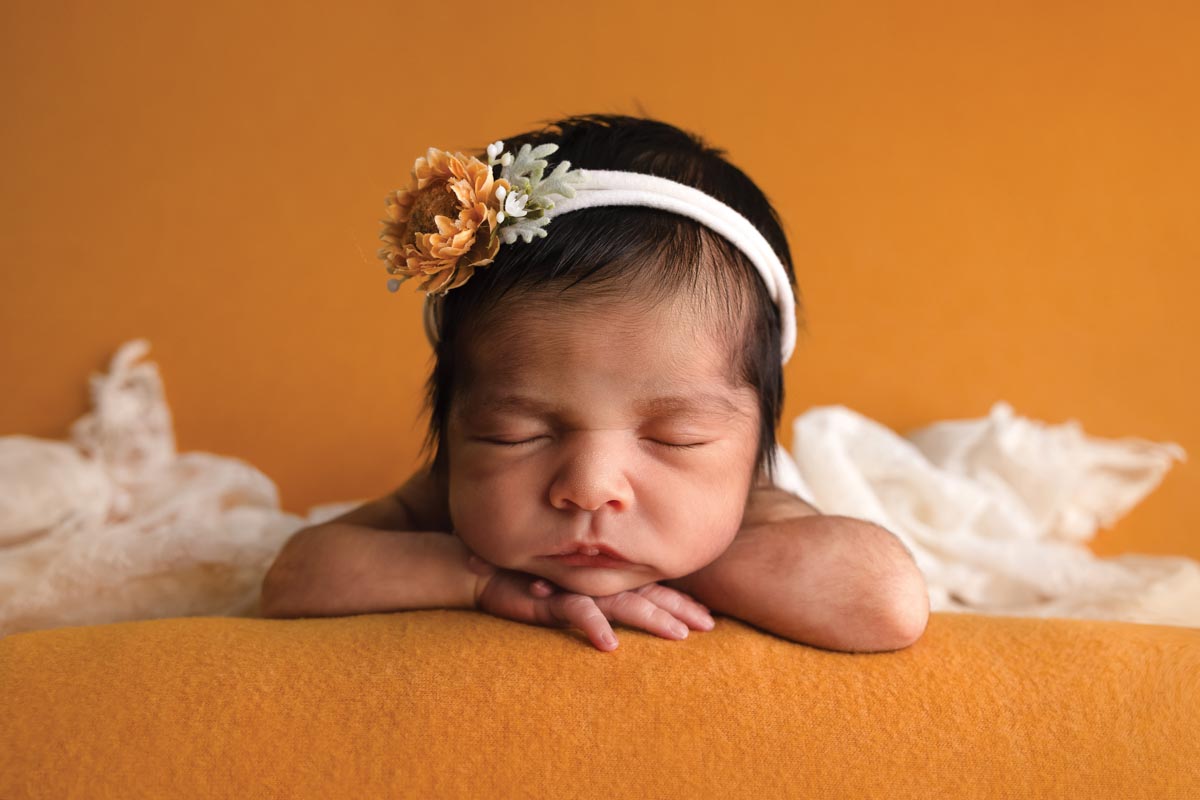 newborn baby wearing white headband with a yellow flower on a yellow background