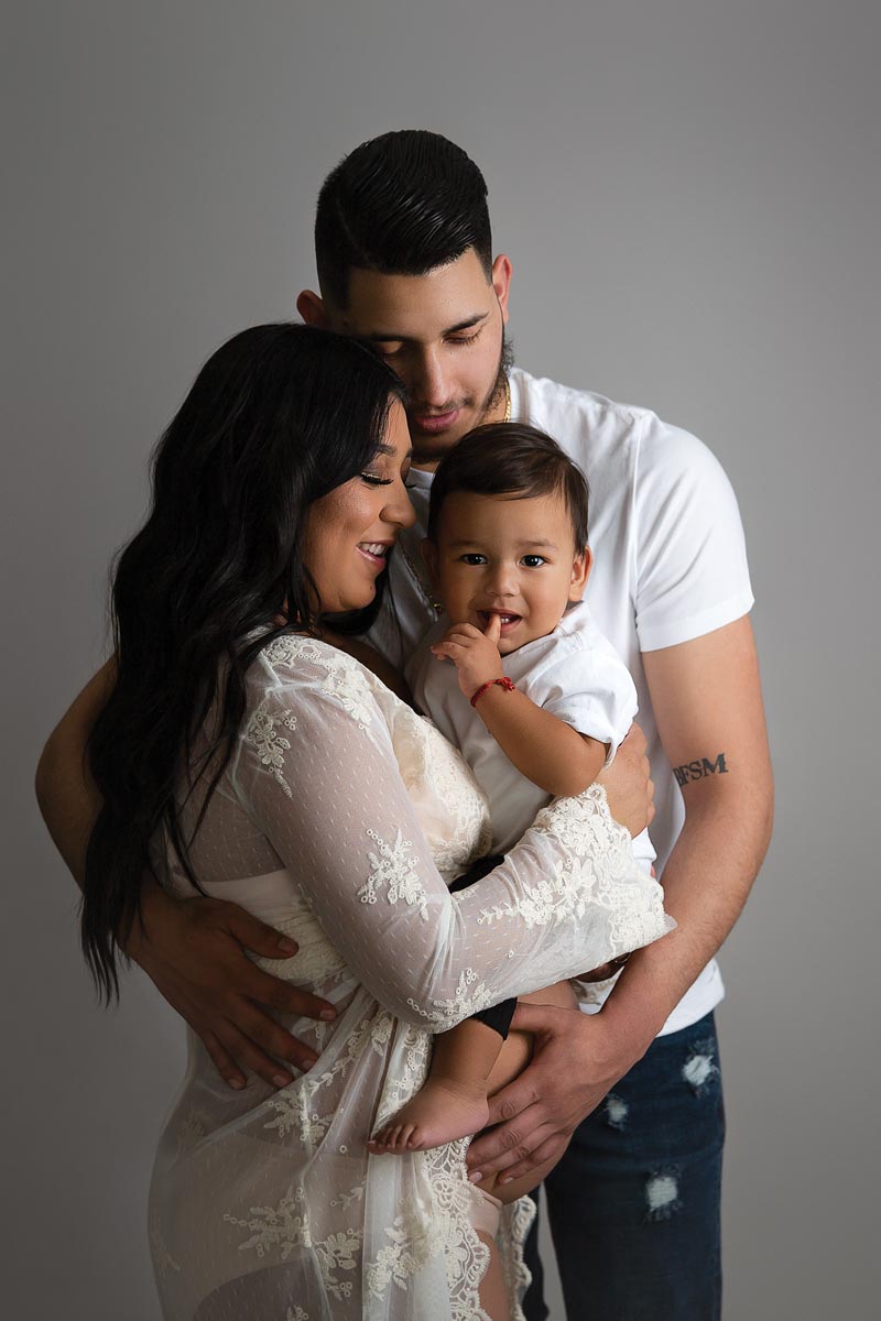 family of three with mom holding son, father hugging them both, and the mom is pregnant