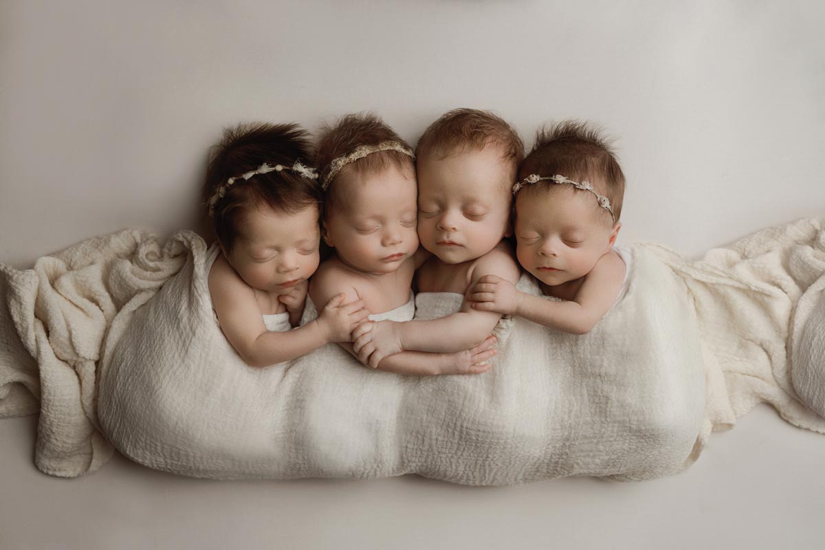four newborn babies with eye clothes sharing a blanket
