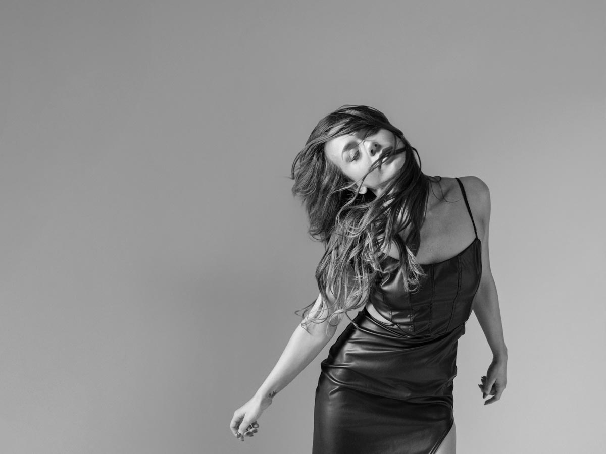 black-and-white photo of a women in a black dress with spaghetti straps dancing with hair across her face