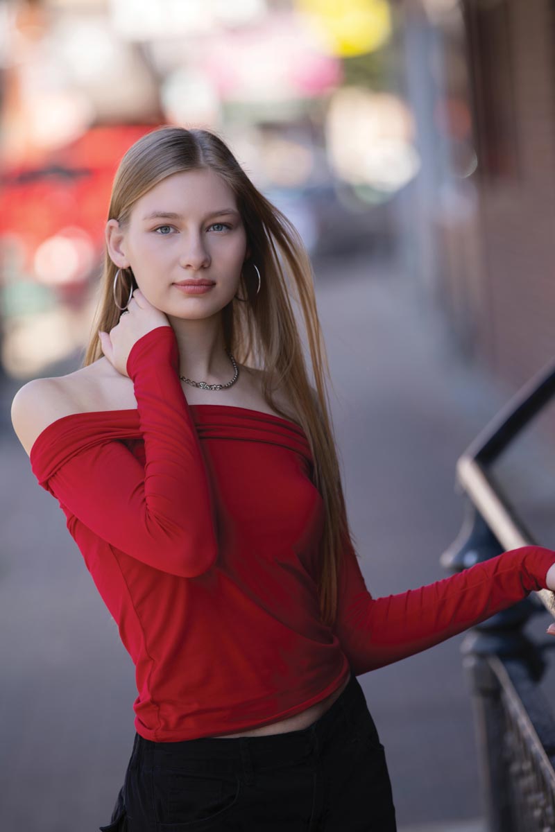 portrait of teenaged girl with blond hair and a red top in an urban setting