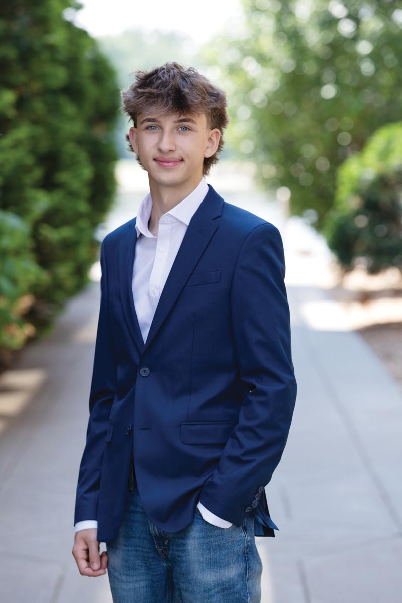 portrait of teenaged boy wearing blue blazer with concrete path and trees in background