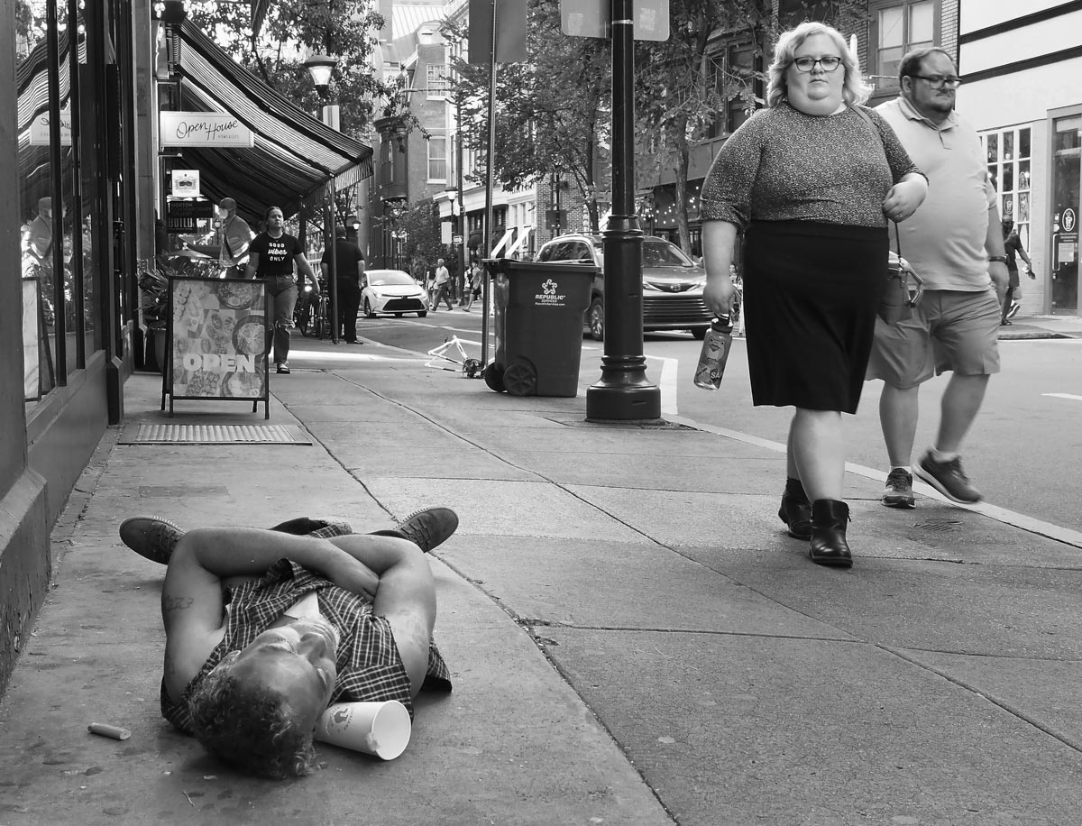 Richard F. Cox's black-and-white photo of a couple walking by a person lying on the sidewalk