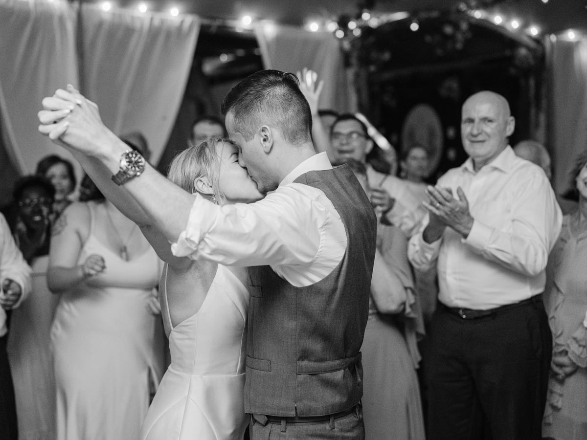 black-and-white photo of a bride and groom kissing on the dance floor with wedding guests in background