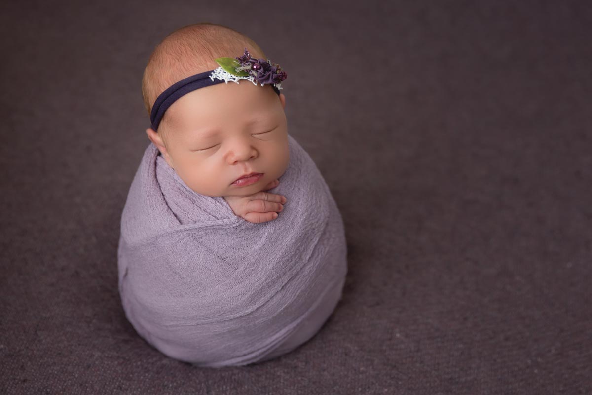 newborn wrapped in lavender fabric wearing a headband