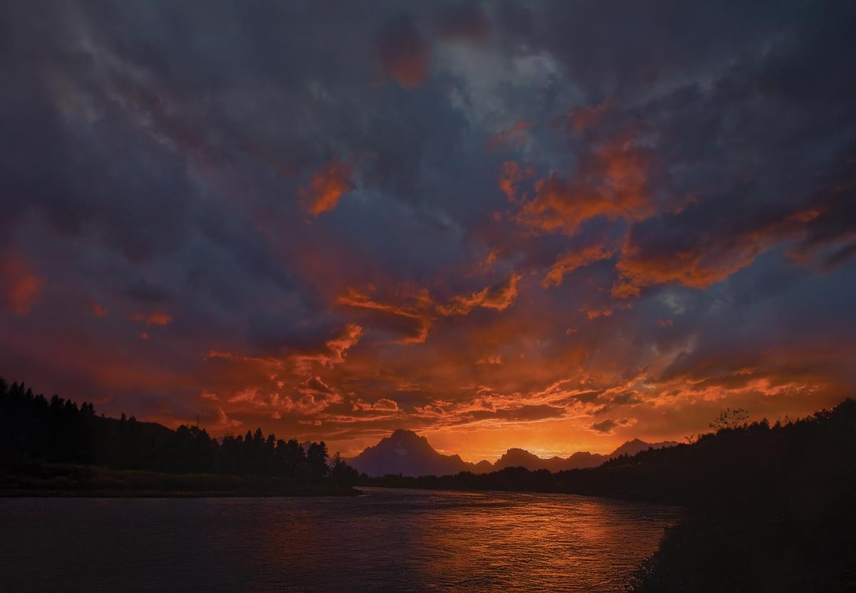 A sun setting over a body of water with a sky full of clouds above