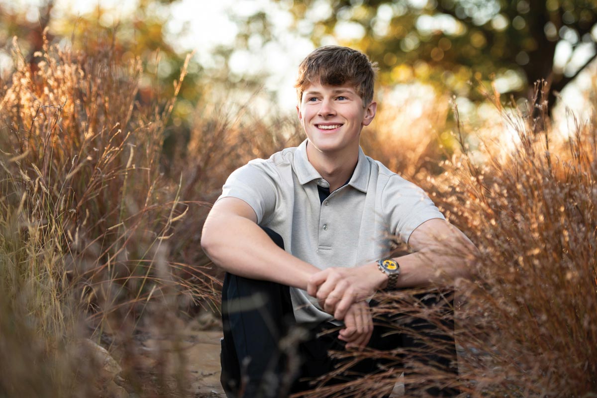 high school senior portrait by Kristina Carlson of a boy sitting on a trail surrounded by tall grass