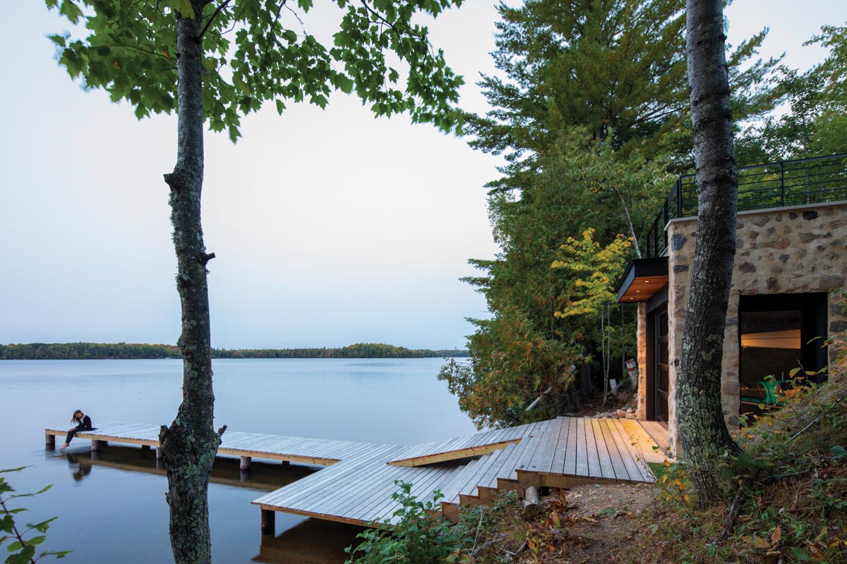 home overlooking a lake with a dock where a women is sitting 
